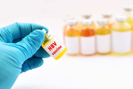 a glove-clad hand holding vaccine bottle with other such small bottles in the background